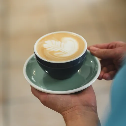 Specialty kávé latte arttal türkiz csészealjon a Manooka Kávézóban, Eger