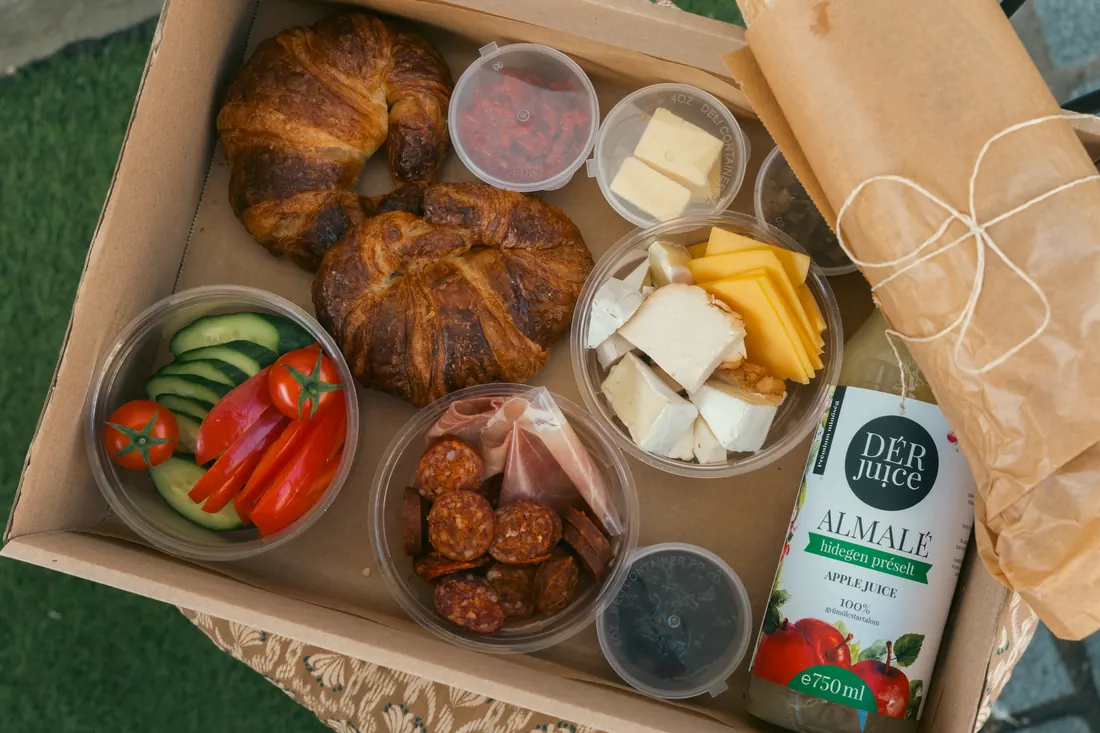 A box felülről: croissant, sajtválogatás, kolbász és sonka, friss zöldség, kencék