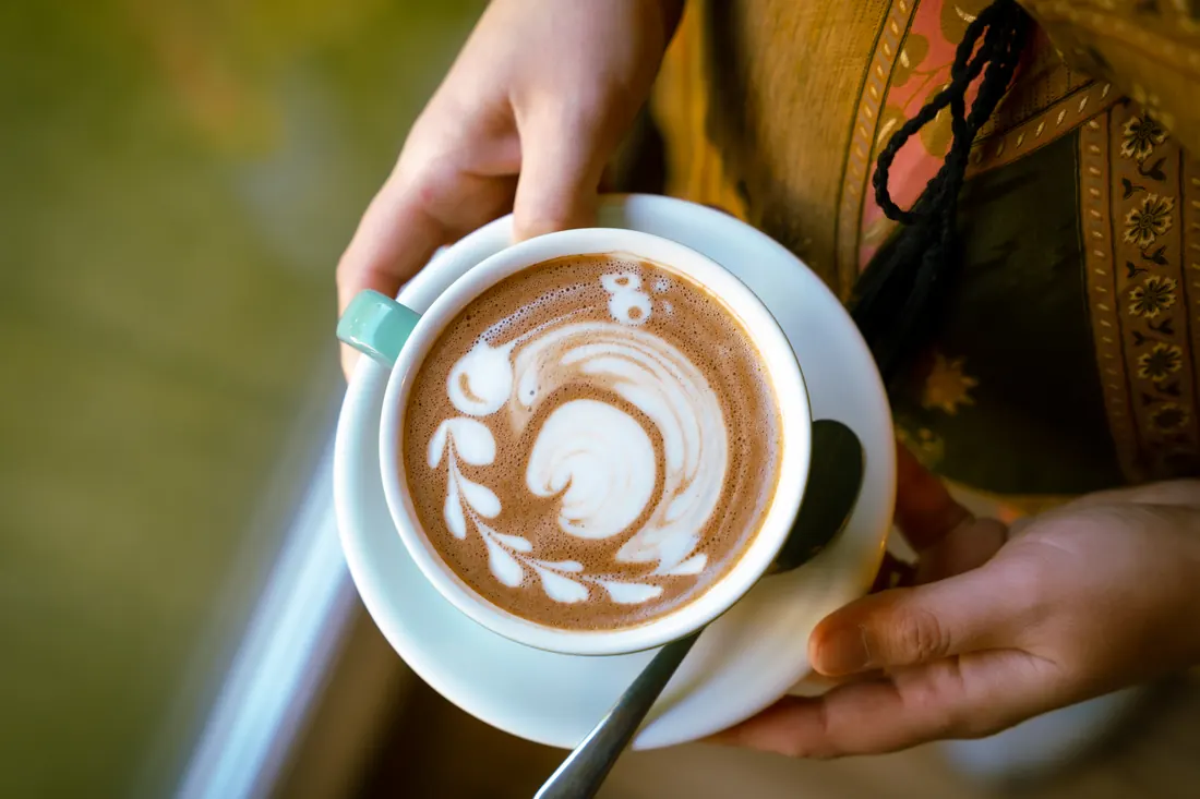 Latte art a csészében, ahogy a barista átnyújtja, Manooka