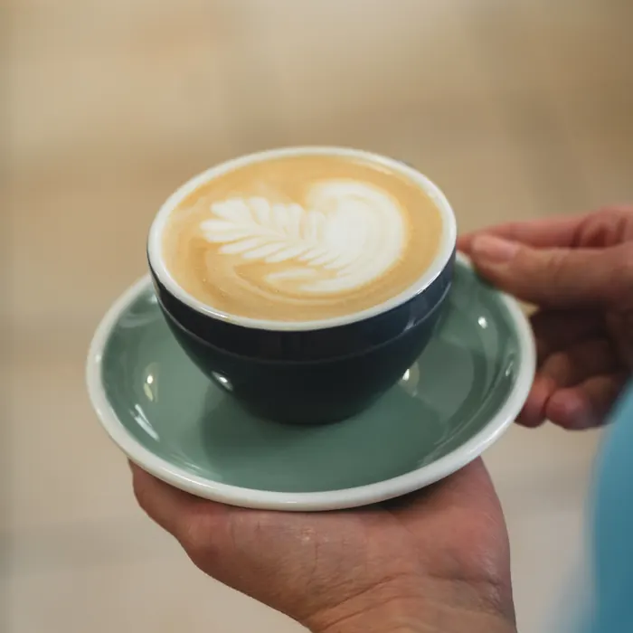 Latte art egy zöld csészében, a barista kezében, Manooka Kávézó